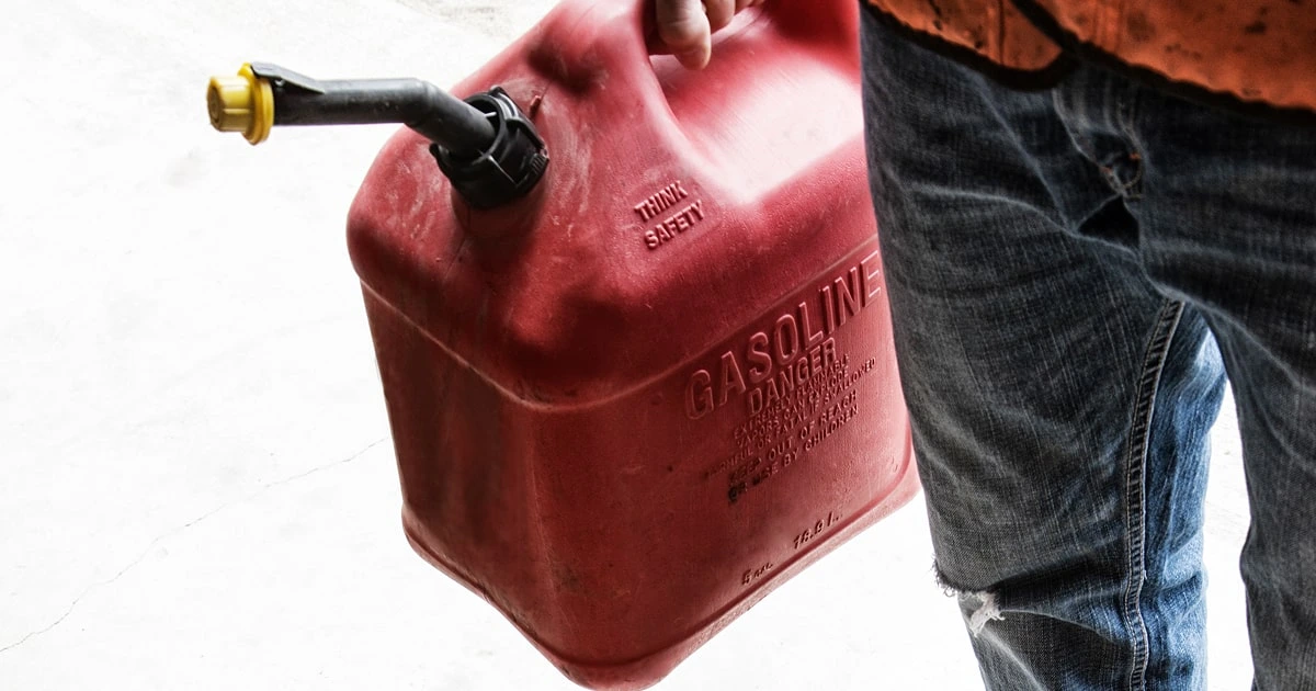 Person carrying red gasoline container with safety warnings