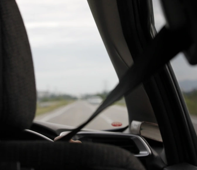 View from inside a moving car with a seatbelt fastened and road ahead