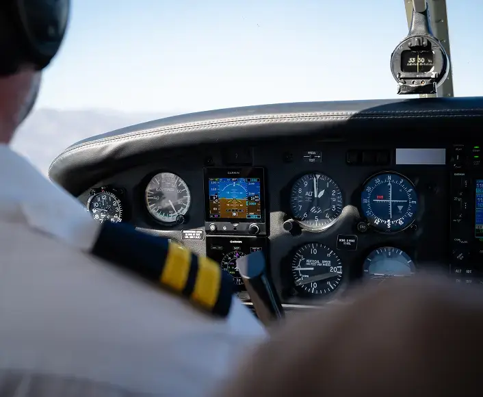 Pilot operating an aircraft cockpit with flight instruments and navigation controls visible during flight.