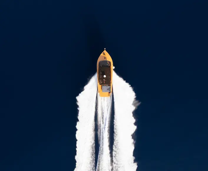 Aerial view of a yellow motorboat speeding across deep blue water, leaving a white wake behind it.