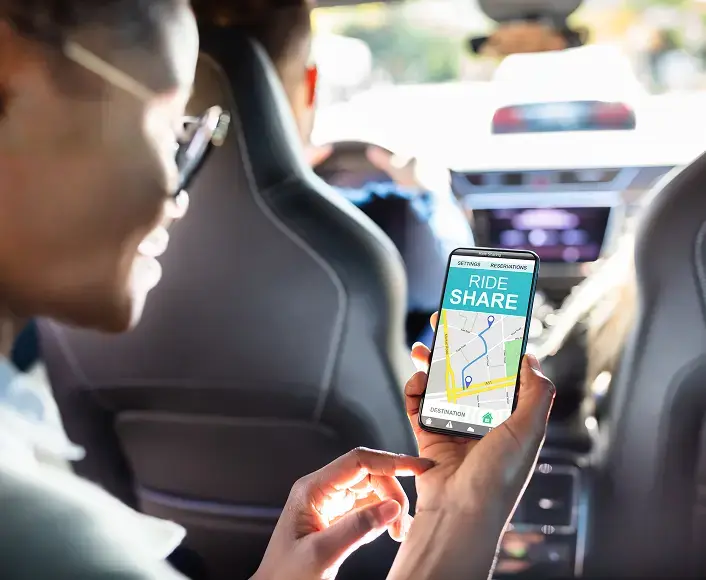 Person using a rideshare app on a smartphone while sitting in the backseat of a car, symbolizing Uber and Lyft accident representation.