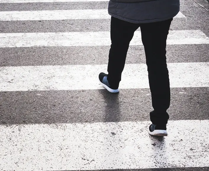 Person walking across a crosswalk, symbolizing pedestrian safety and awareness on city streets.