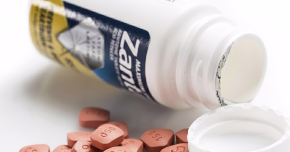 Zantac bottle tipped over with pills spilled out beside an open cap.